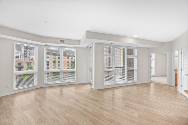 Bright, empty modern apartment with large windows, light wood floors, and white walls.