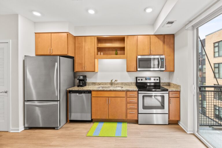 Modern kitchen with stainless steel appliances, wood cabinets, and a striped rug in front of the sink.