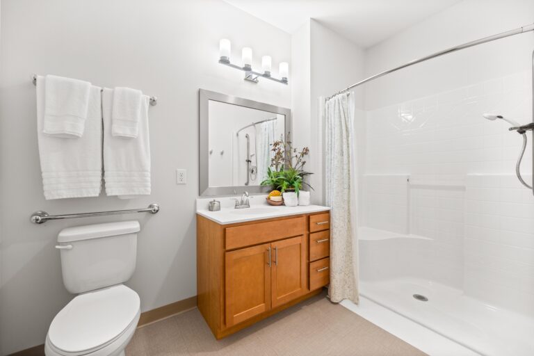 Modern bathroom with a wooden vanity, large mirror, white towels, and a walk-in shower with a curtain.