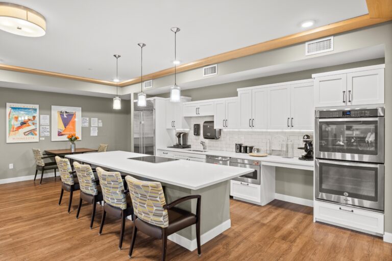 Modern kitchen with white cabinets, island seating, pendant lights, and wood-style flooring.