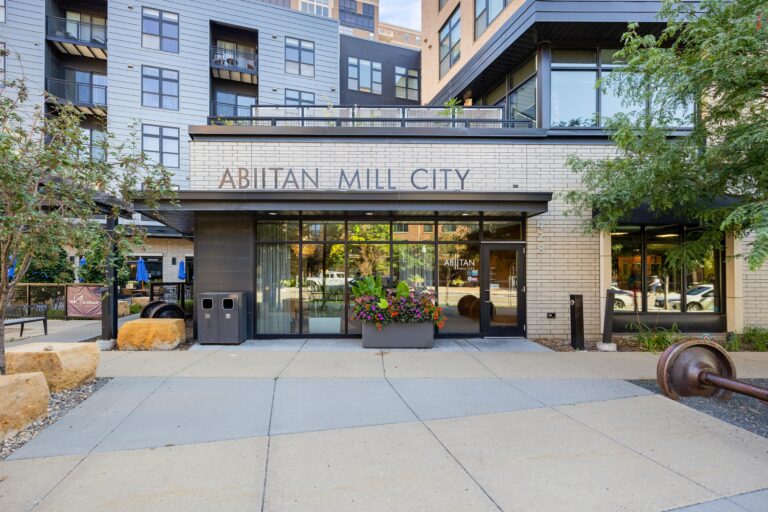 Entrance of Abitan Mill City building with large windows, potted flowers, and modern architecture.