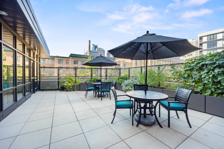 Spacious rooftop patio with tables, chairs, umbrellas, and city buildings in the background.