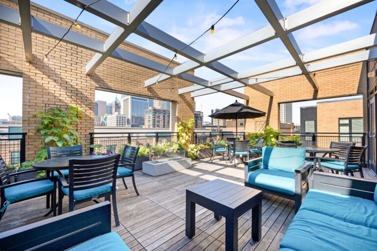 Rooftop patio with seating, tables, string lights, plants, and city buildings in the background.