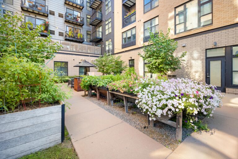 Raised garden beds with flowers and greenery in a modern apartment courtyard with balconies above.