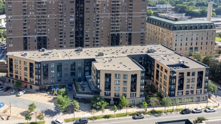 A modern apartment complex with large windows and a courtyard, surrounded by city streets and parking.