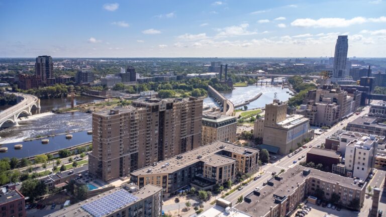 Aerial view of a cityscape with a river, bridges, and high-rise buildings under a blue sky.