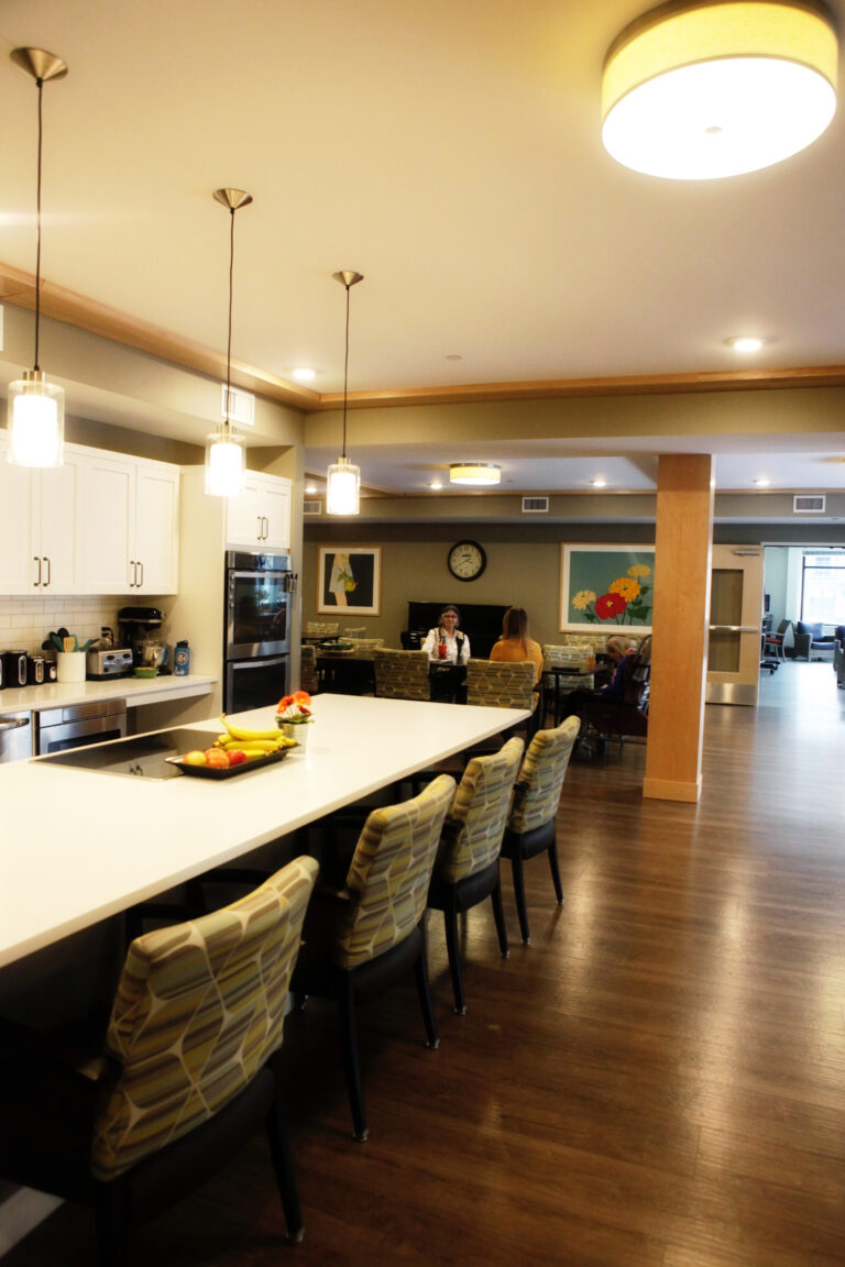 Modern communal kitchen with pendant lights, chairs, and people sitting at tables in the background.