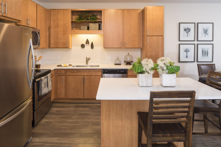 Modern kitchen with wood cabinets, stainless steel appliances, and potted plants on a white island countertop.