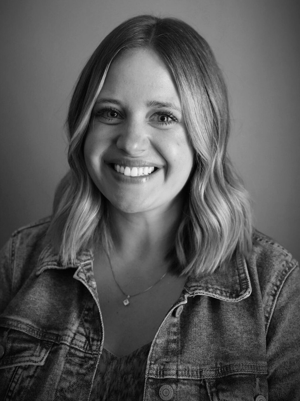 Black and white portrait of Kristin Pillsbury with shoulder-length blonde hair wearing a jean jacket over blouse.