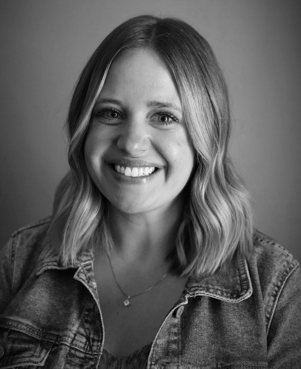 Black and white portrait of Kristin Pillsbury with shoulder-length blonde hair wearing a jean jacket over blouse.