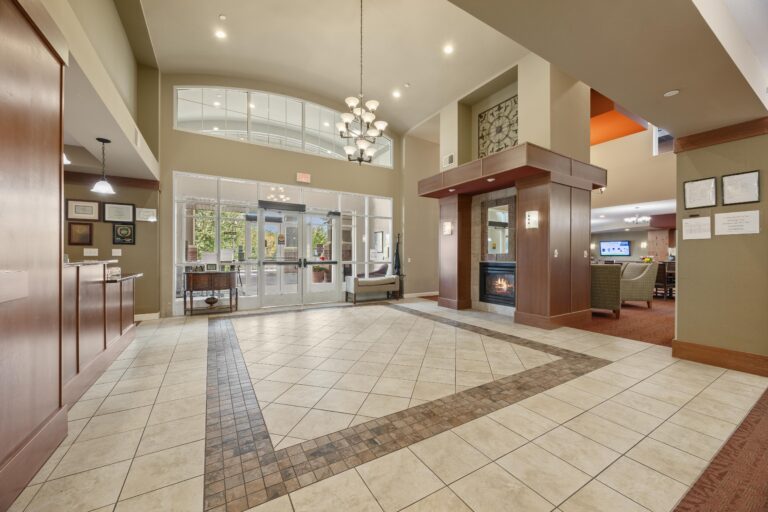 Spacious lobby with tiled floors, chandelier, fireplace, and seating area near glass entrance doors.