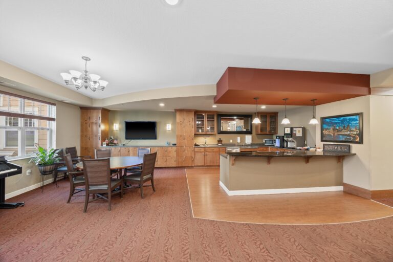 Spacious lounge area with wood cabinets, TV, dining table, and a bar counter under pendant lights.
