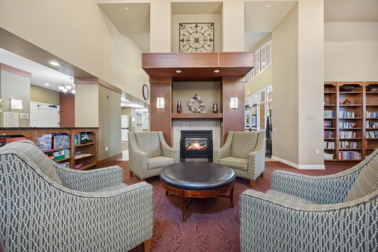 Four patterned armchairs surround a round ottoman in a cozy lounge with a fireplace and bookshelves.