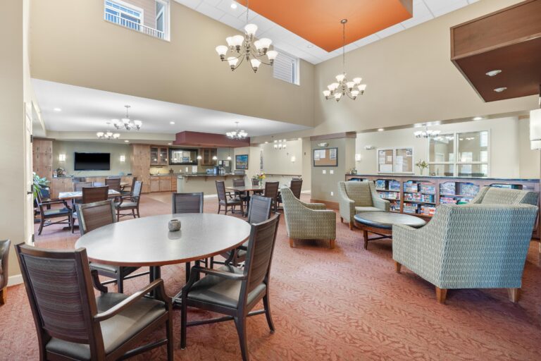 Spacious lounge with tables, chairs, armchairs, chandeliers, and a snack bar in a bright, open room.