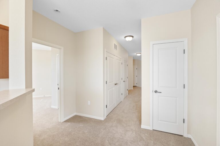 Bright hallway with beige carpet, white doors, and cream walls in a modern, empty home interior.