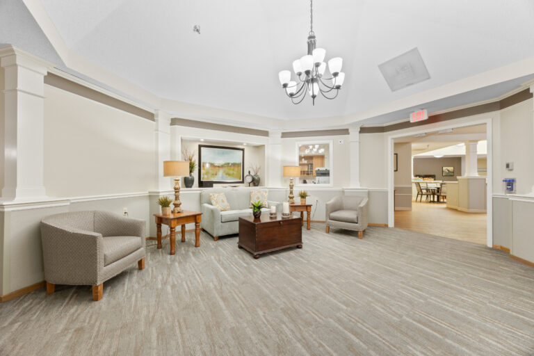 A bright, modern lounge area with armchairs, a sofa, and a chandelier in a neutral color palette.