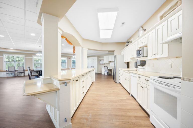 Spacious kitchen with white cabinets and wood flooring, connected to a large dining area.
