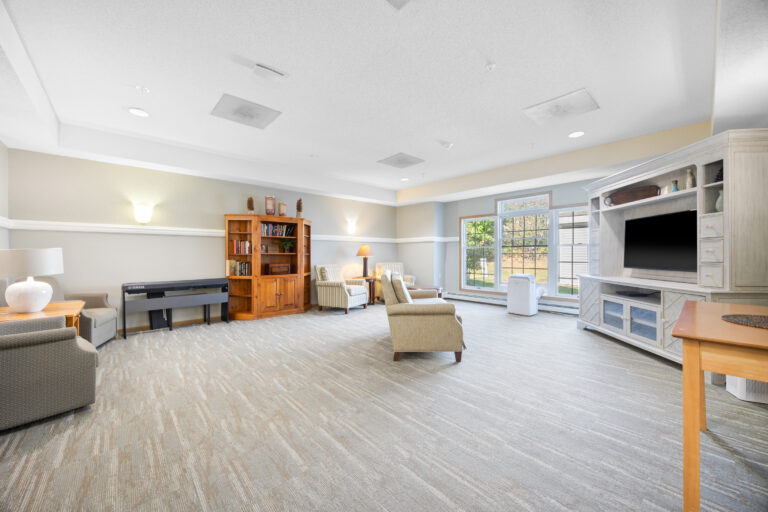 Bright, spacious living room with armchairs, bookshelves, a TV, large window, and neutral decor.