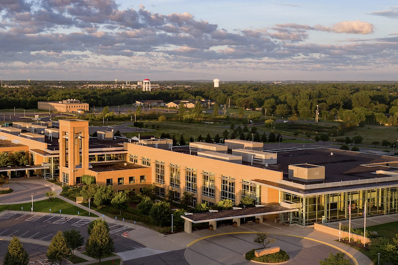 Aerial photo of a modern building made of yellow stone facade and glass, featuring large window sections and two round-a-about driveway drop-offs with carports.