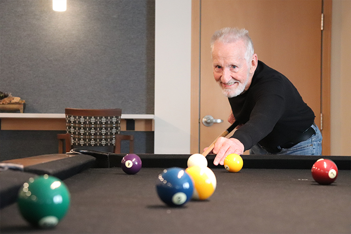 Older gentleman lining up a shot on a billiards table.