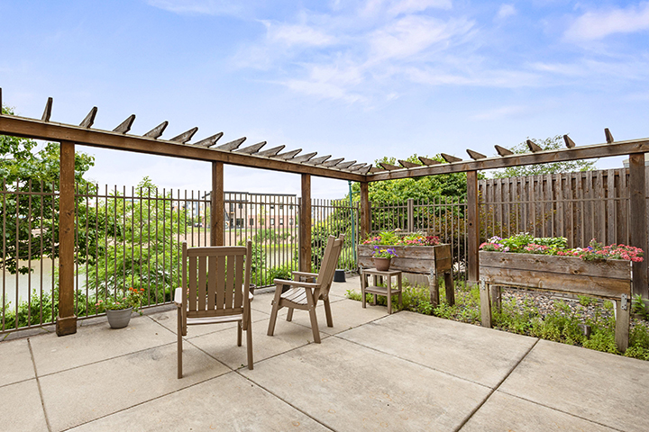 A secured outdoor patio with seating, raised garden beds, and pergola surrounded by trees.