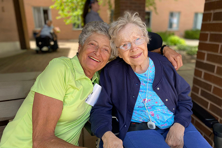 An older woman with her arm wrapped around another older woman. They are smiling.