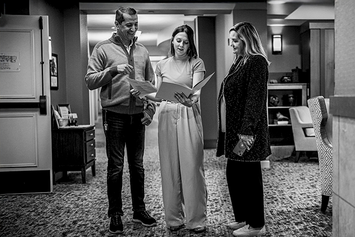 Black and white indoor photo of three administrators, one male and two female, reviewing the contents of a folder.