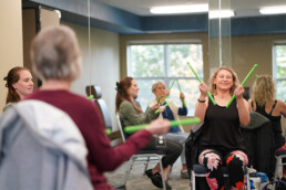Multiple women sit in a mirrored studio taking part in a group music activity.
