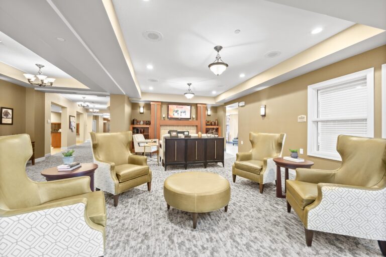 Four high-back lounge chairs encircle a matching round ottoman; positioned adjacent to a credenza and sofa facing a modern fireplace hearth.