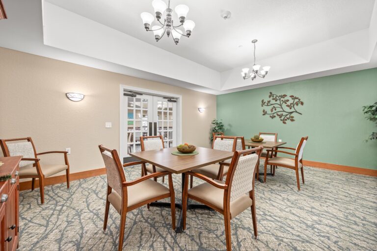 Bright, carpeted room with one cream wall and one sage green wall; two four-person dining tables with upholstered arm chairs; closed french doors connecting to main dining room.