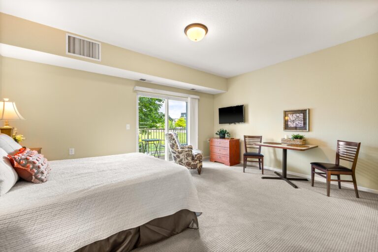 Large, carpeted living area with bed, table and chairs, lounge chair and sliding glass door to private balcony.