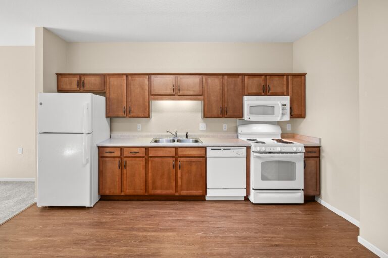 The full kitchen space with wood flooring, white refrigerator, range, microwave, and dishwasher appliances and stained wood cabinetry.