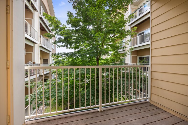 Private balcony with cream metal railing, overlooking building courtyard, neighboring balconies and trees.