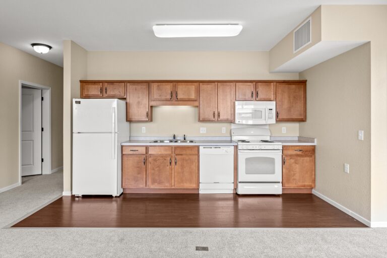 The full kitchen space with wood flooring, white refrigerator, range, microwave, and dishwasher appliances and stained wood cabinetry.