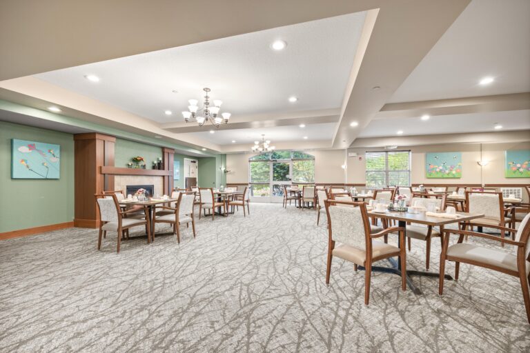 Large, carpeted dining room featuring a gas fireplace, 4-person tables and upholstered chairs, large windows, and plenty of light.