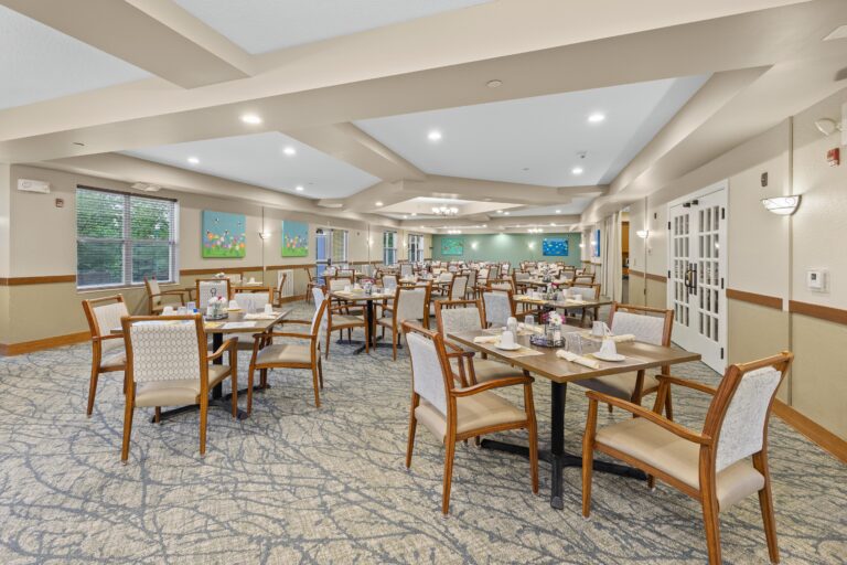 Large, carpeted dining room with 4-person tables and upholstered chairs, large windows, and plenty of light.