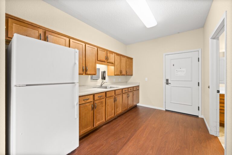 Apartment entry to kitchenette with sink, countertop, wood cabinets and full-size refrigerator.