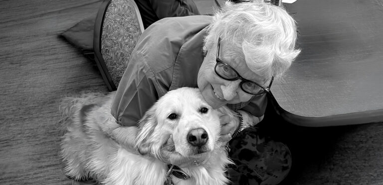 A senior woman smiling and hugging a golden retriever volunteer named Bella. Bella’s visits bring comfort and smiles!