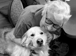 A senior woman smiling and hugging a golden retriever volunteer named Bella. Bella’s visits bring comfort and smiles!