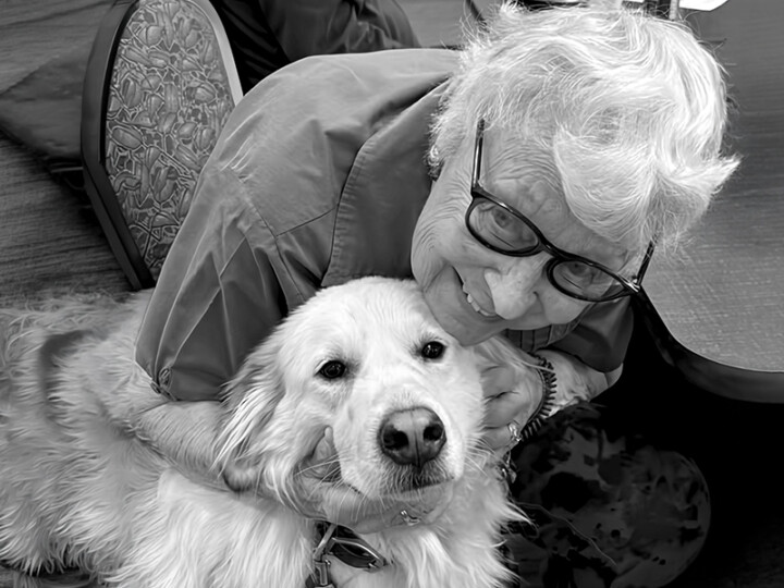A senior woman smiling and hugging a golden retriever volunteer named Bella. Bella’s visits bring comfort and smiles!