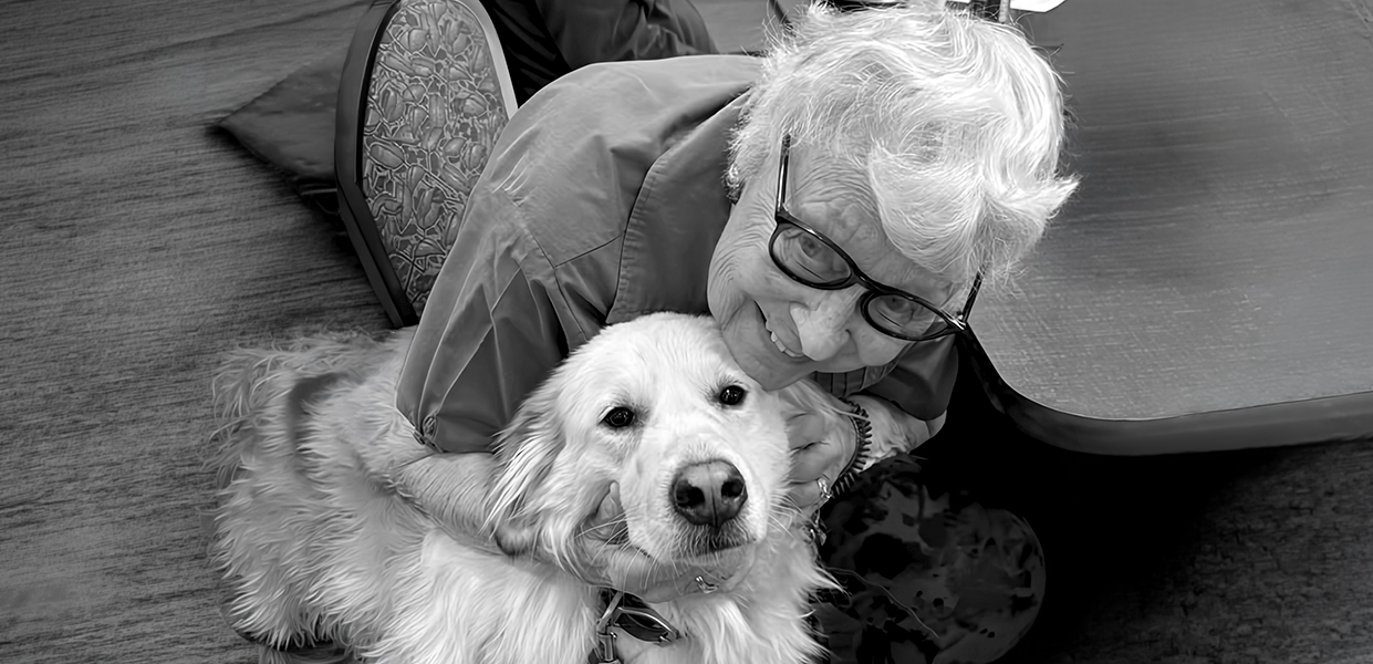 A senior woman smiling and hugging a golden retriever volunteer named Bella. Bella’s visits bring comfort and smiles!