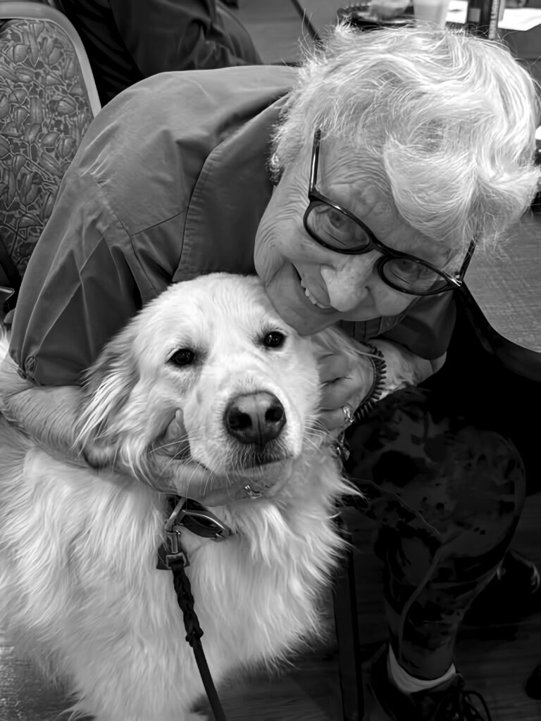 A senior woman smiling and hugging a golden retriever volunteer named Bella. Bella’s visits bring comfort and smiles!