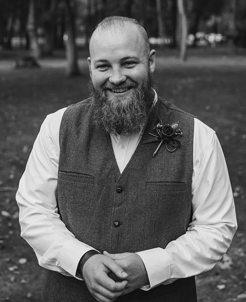 Professional black and white portrait of Jordan Thompson, wearing a button shirt, wool vest and flower corsage on his lapel