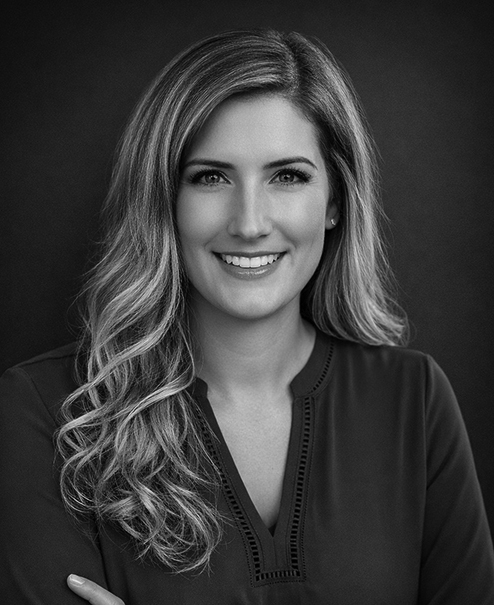 Professional black and white portrait of Kelsey Bibeau, wearing a v-neck sweater jacket