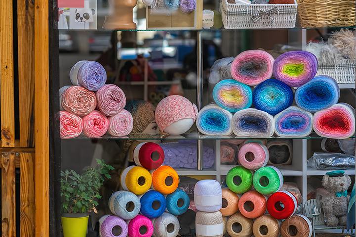 Bundles of colorful yarn, thread and fabric stacked in pyramid shape in a craft shop window.