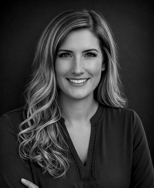 Professional black and white portrait of Kelsey Bibeau, wearing a v-neck sweater jacket
