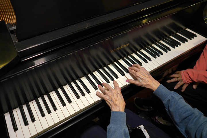 Overhead view of an older person's arms outstreched with fingers resting on the keys of a piano.