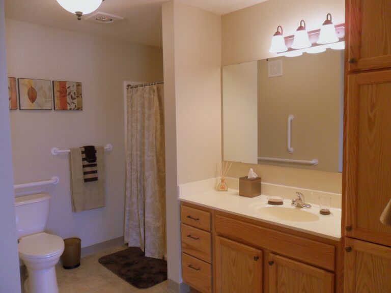 An apartment bathroom with wooden cabinets and cream-colored vanity.