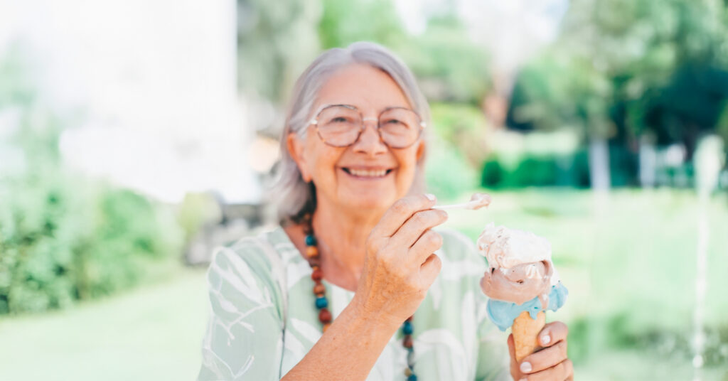 An older woman with glasses smiles while holding an ice cream cone