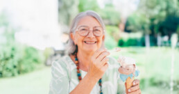 An older woman with glasses smiles while holding an ice cream cone